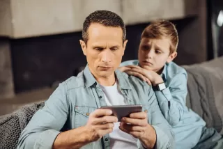 Pai olhando para o celular enquanto o filho está frustrado